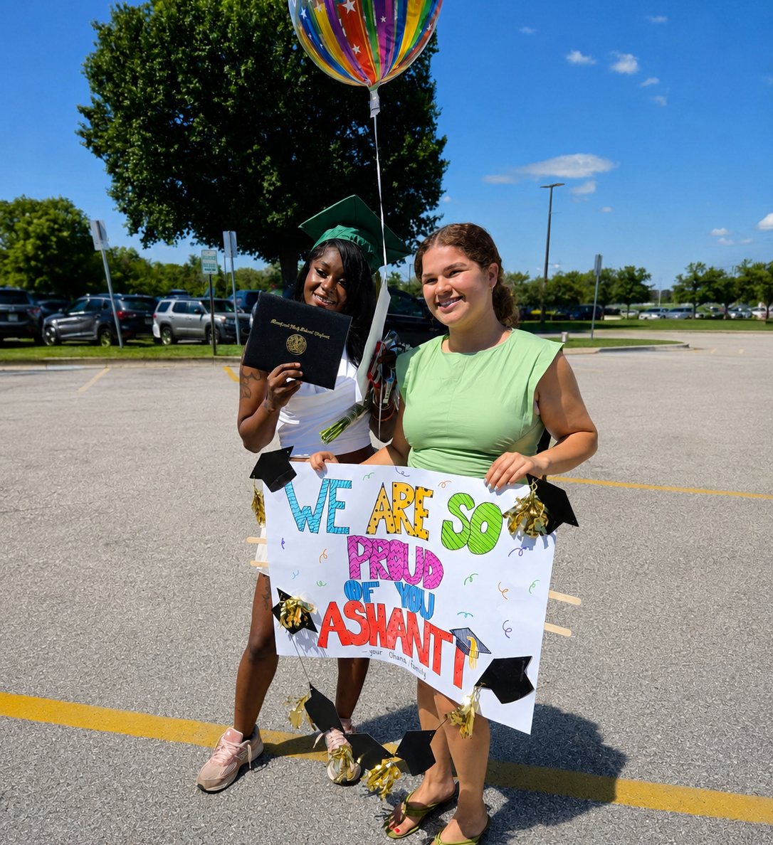 An OhanaHC graduate in her cap and gown holding her diploma beside her mentor, who holds a hand lettered sign reading We are so proud of you Ashanti.