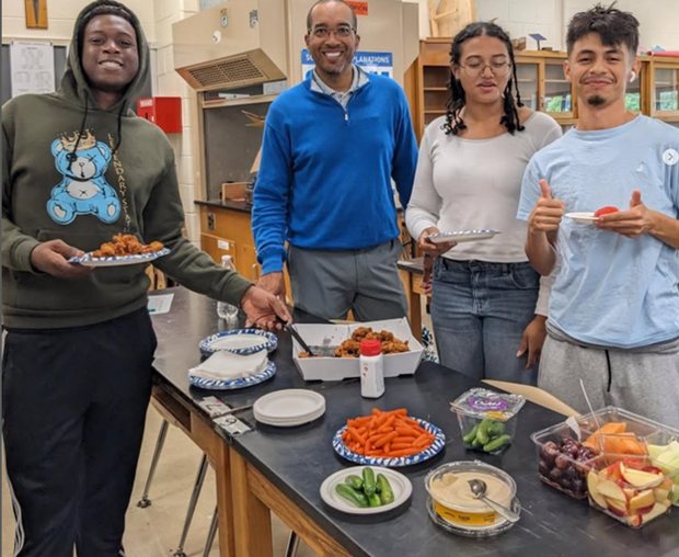 OhanaHC students and mentors gathered around a table of food at an after-school club meeting.