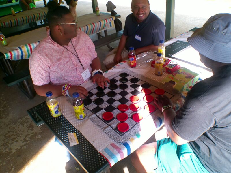 An OhanaHC student playing giant checkers with two adults at the 2026 year end celebration