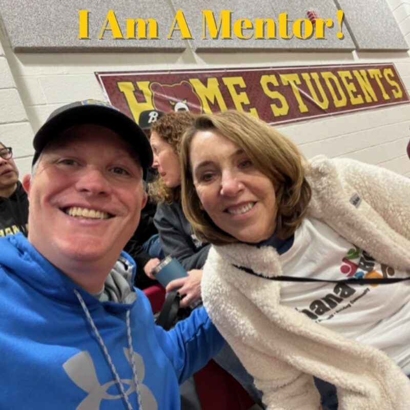 Two OhanaHC mentors smiling in a selfie under a sign that reads I Am A Mentor.