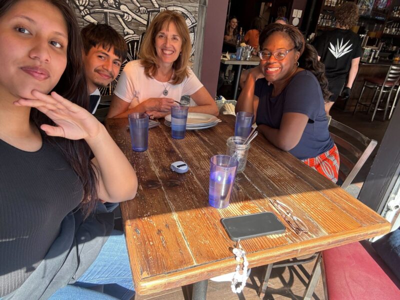 Two OhanaHC students and their two mentors around a restaurant table, all smiling at the camera
