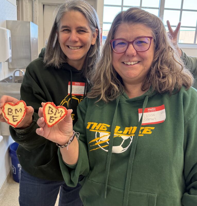 Two OhanaHC mentors holding up the heart shaped cookies they decorated