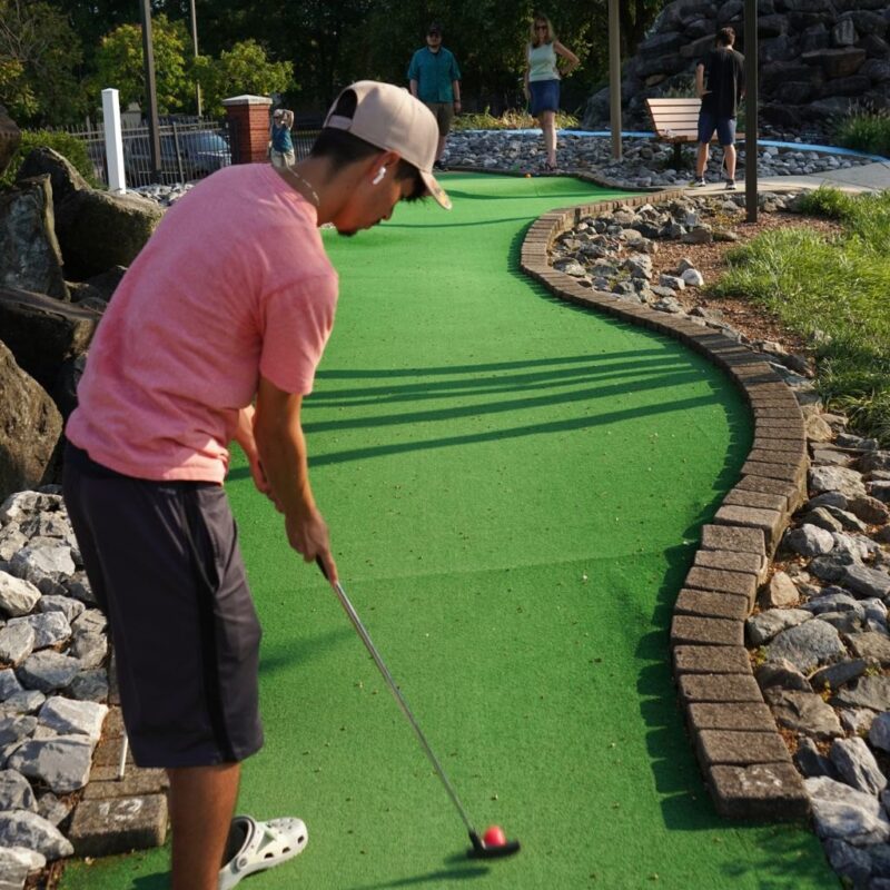 An OhanaHC student lining up a putt on a mini golf course during an outing