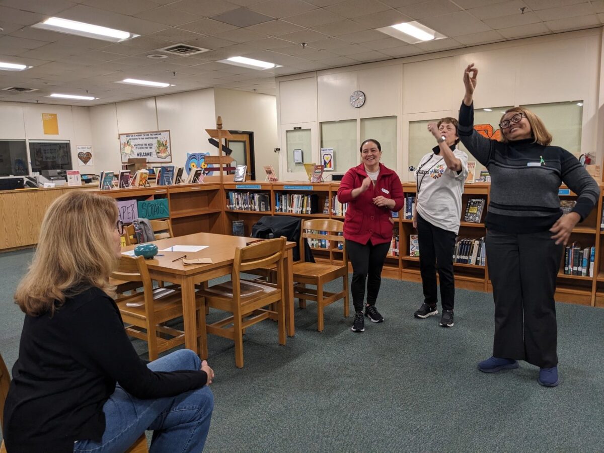 An OhanaHC adult and students working together around tables in a school library