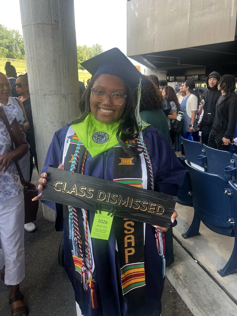 A Guilford Park High School graduate in cap and gown at the 2026 commencement, holding a sign reading Class Dismissed