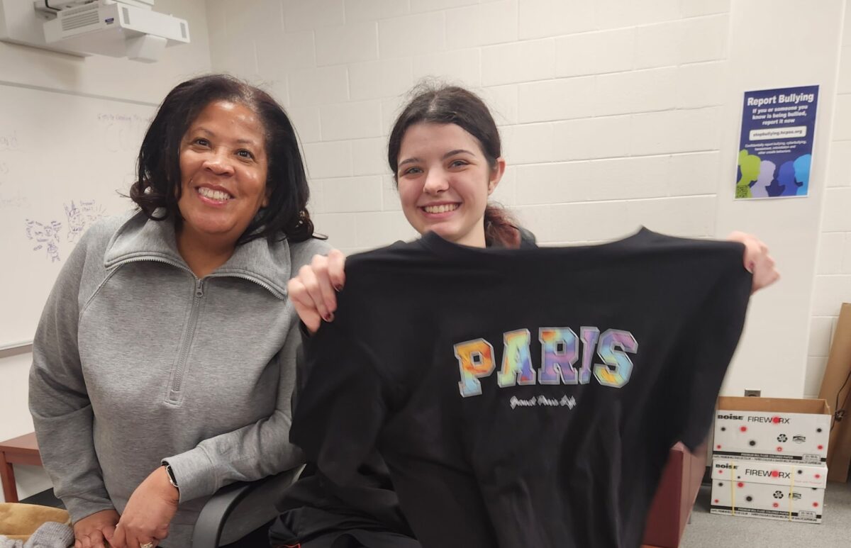 An OhanaHC mentor and her student smiling as they hold up a Paris shirt.
