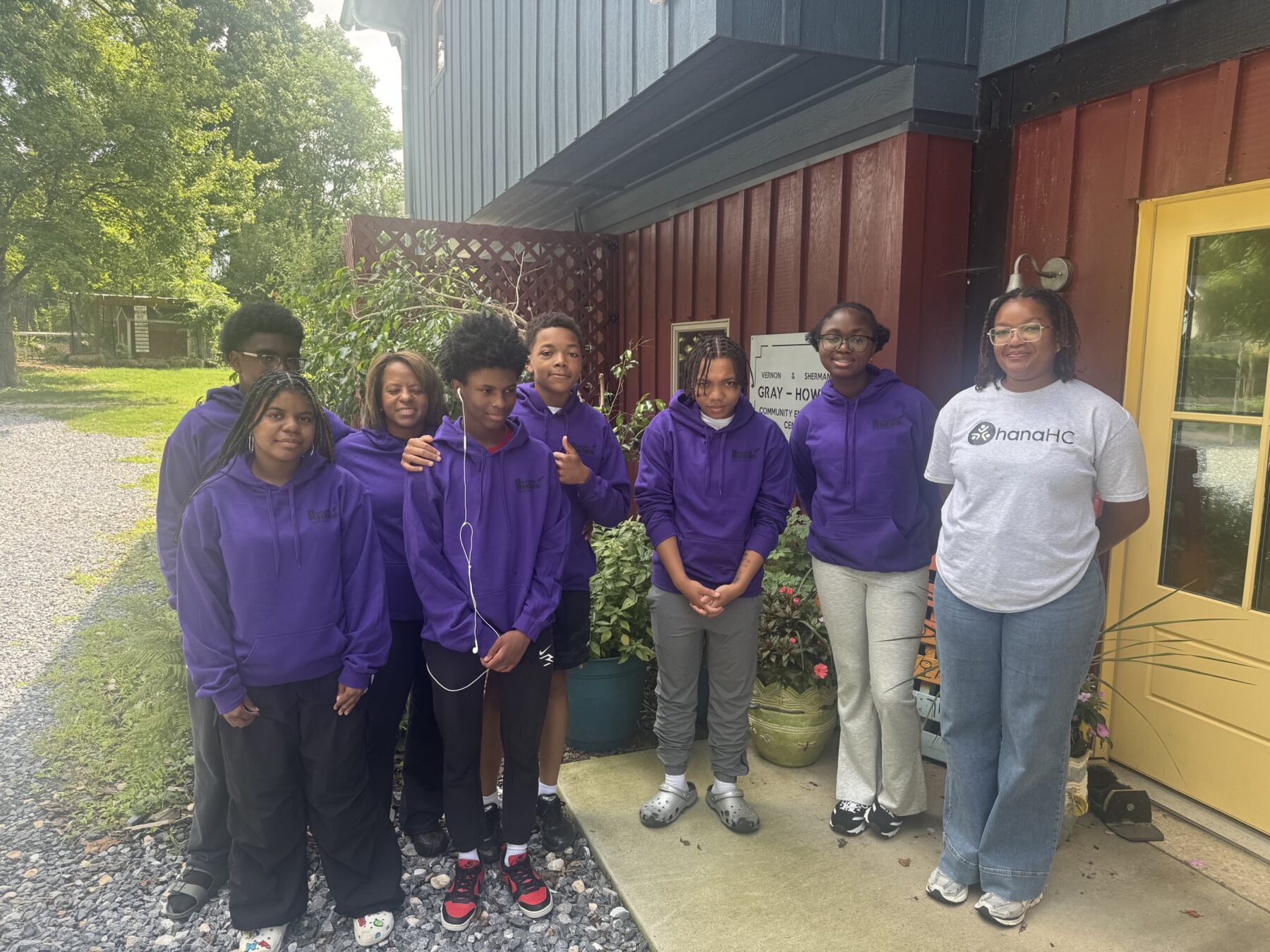 OhanaHC students in purple shirts with their program leaders outside a lodge during a summer program.