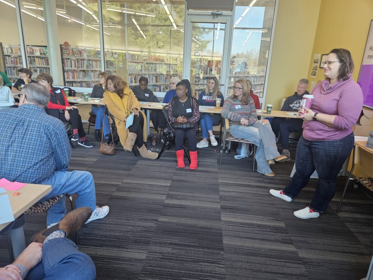 An OhanaHC leader speaking to a circle of adults in a library meeting room