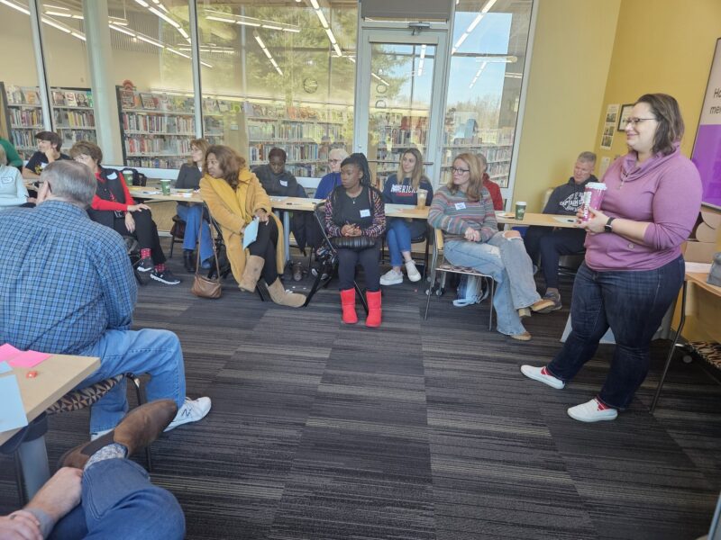 An OhanaHC leader speaking to a circle of adults in a library meeting room