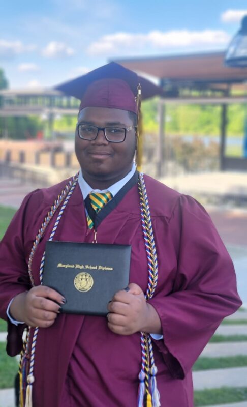 Michael B., a Hammond High School graduate ready for Kutztown University, in his cap, gown and cords holding his diploma.