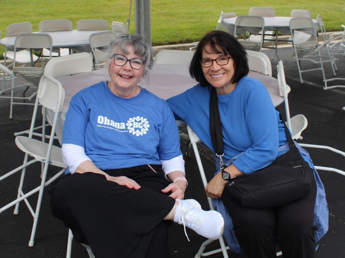 Two OhanaHC volunteers in OhanaHC shirts smiling together under a tent at an OhanaHC event