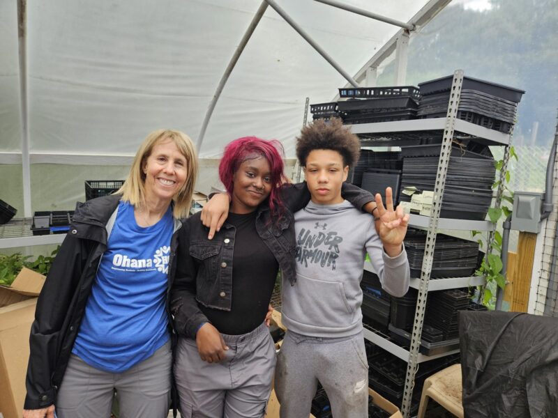 An OhanaHC volunteer in a branded shirt standing with two students at a community event
