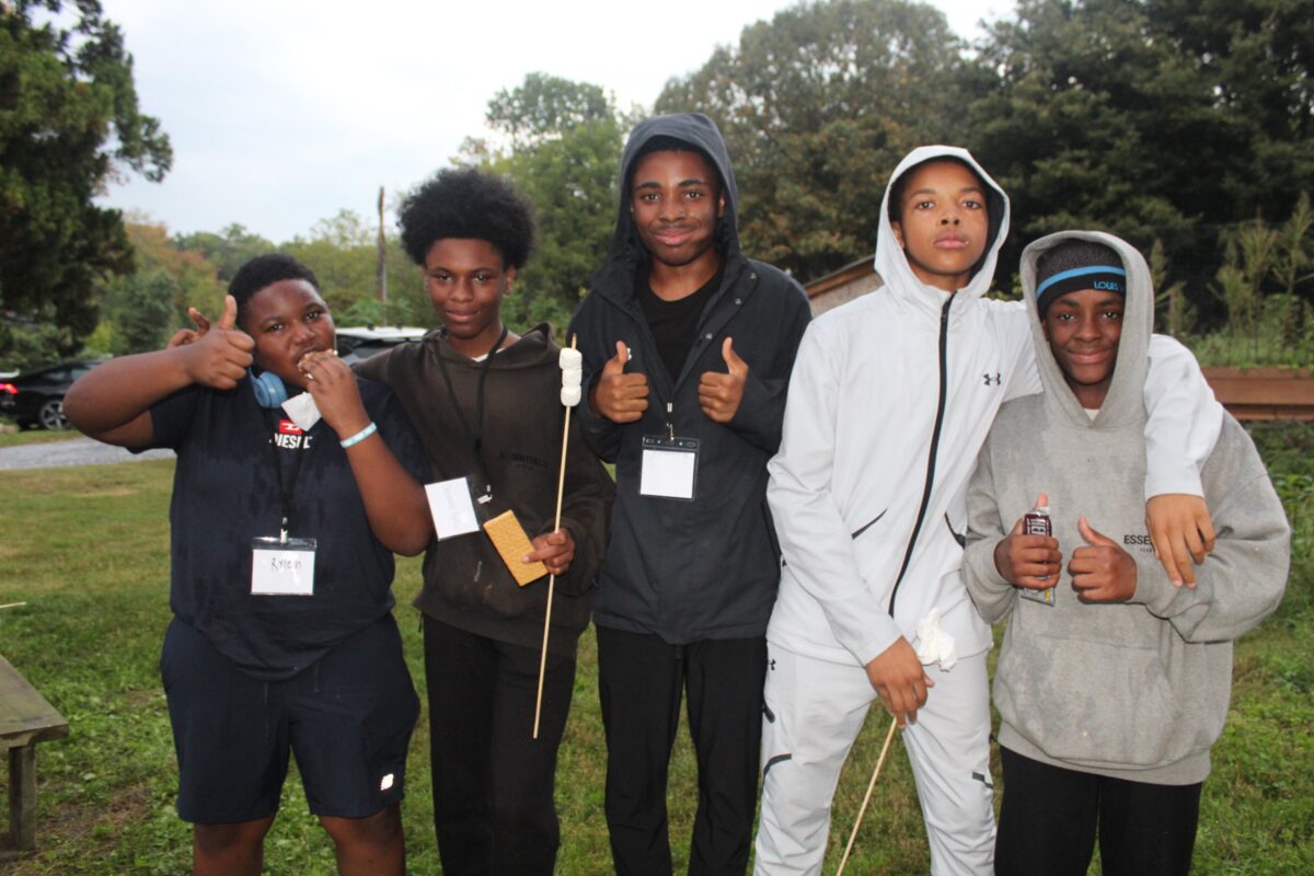 Five OhanaHC students giving a thumbs up at the fall bonfire, one holding a marshmallow stick