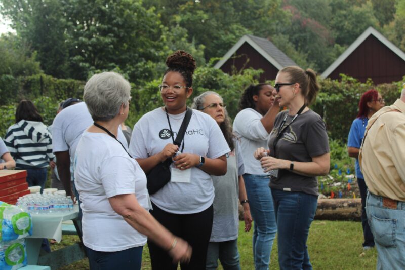 OhanaHC volunteers in OhanaHC shirts talking and laughing on the lawn at an outdoor event